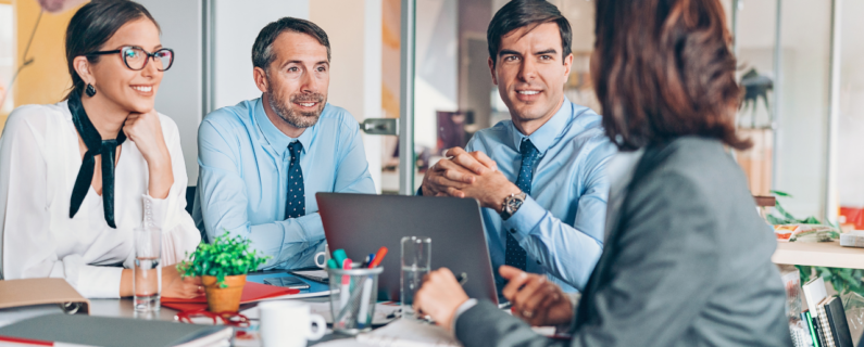 Property Management Four professionals in business attire sit at a table during a meeting, with laptops, notebooks, and water glasses visible